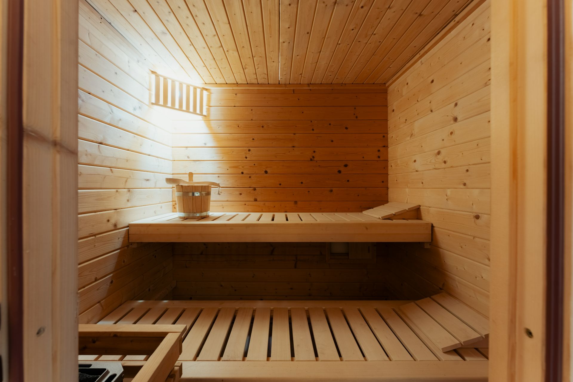 Holzsauna mit zwei Sitzbänken und einem Eimer auf der oberen Bank.