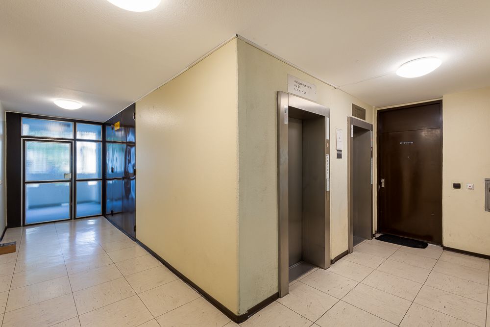 Hausflur mit zwei Aufzügen, brauner Tür und Glaseingangstür.