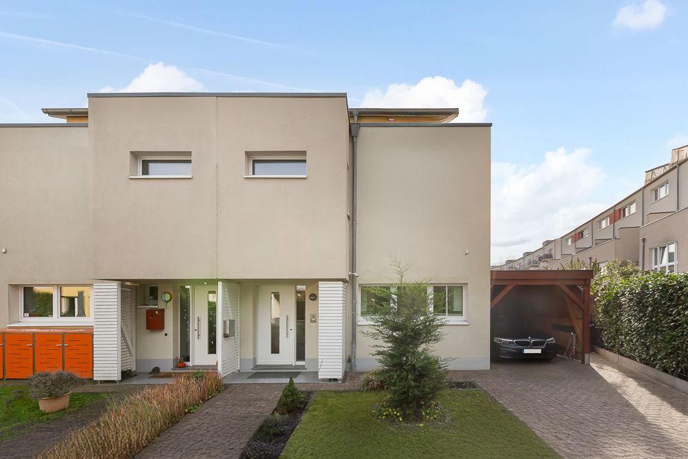 Vorderansicht eines modernen Doppelhauses mit Vorgarten und Carport.