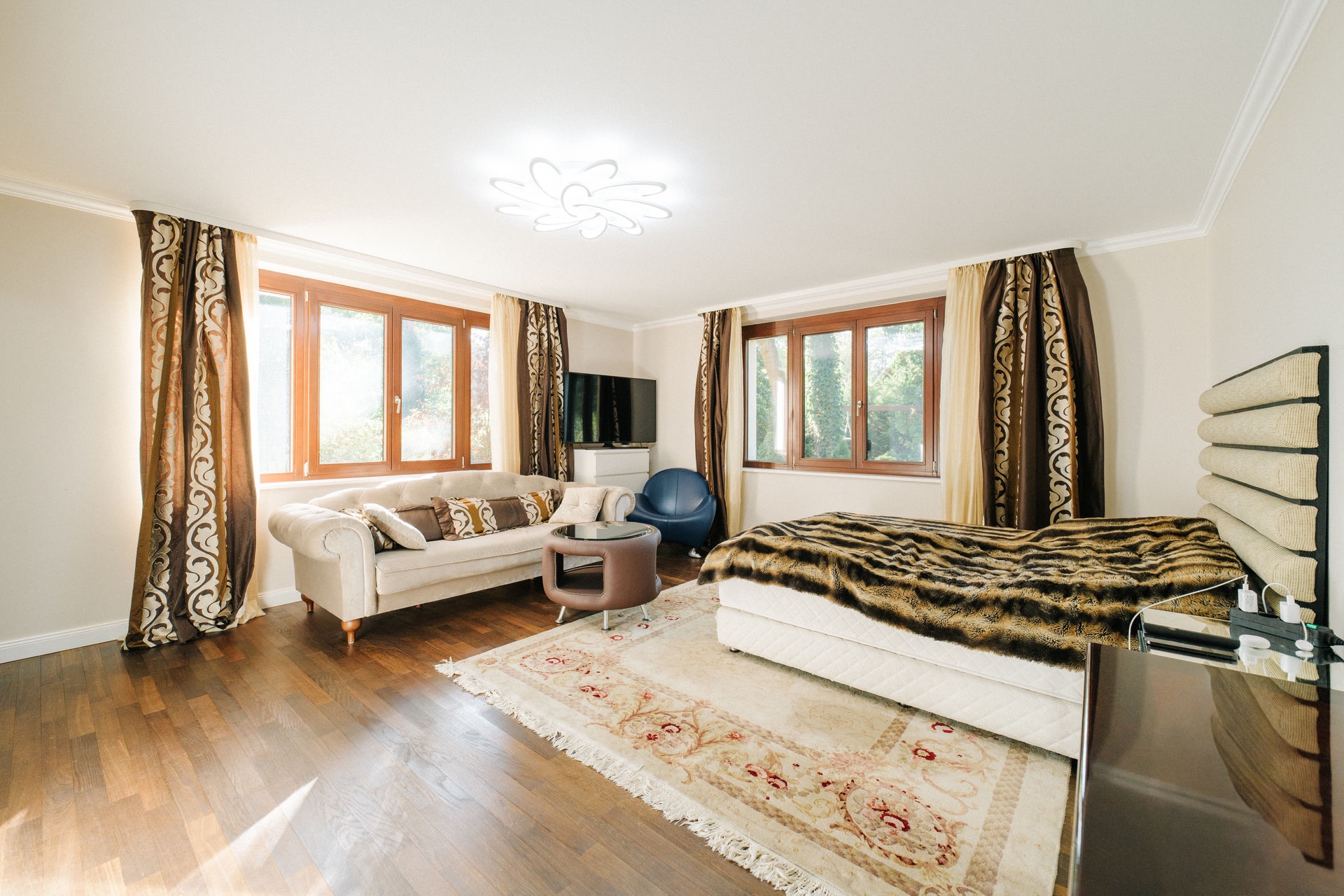 Helles Schlafzimmer mit Sofa, Teppich, Bett und großen Fenstern mit Vorhängen.