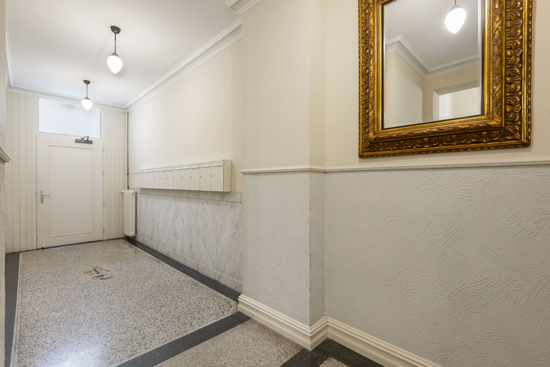 Heller Flur mit Briefkästen, Tür am Ende und einem großen Spiegel an der Wand.