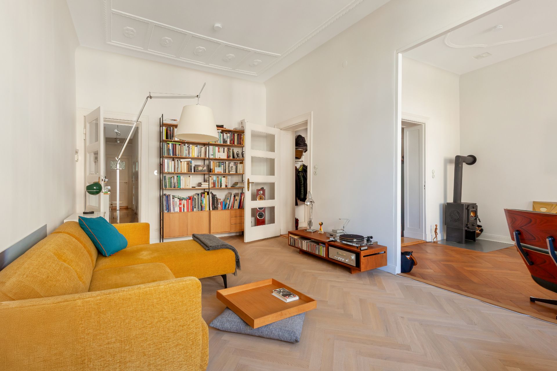Helles Wohnzimmer mit gelbem Sofa, Bücherregal, Plattenspieler und Blick in einen Raum mit Kamin.