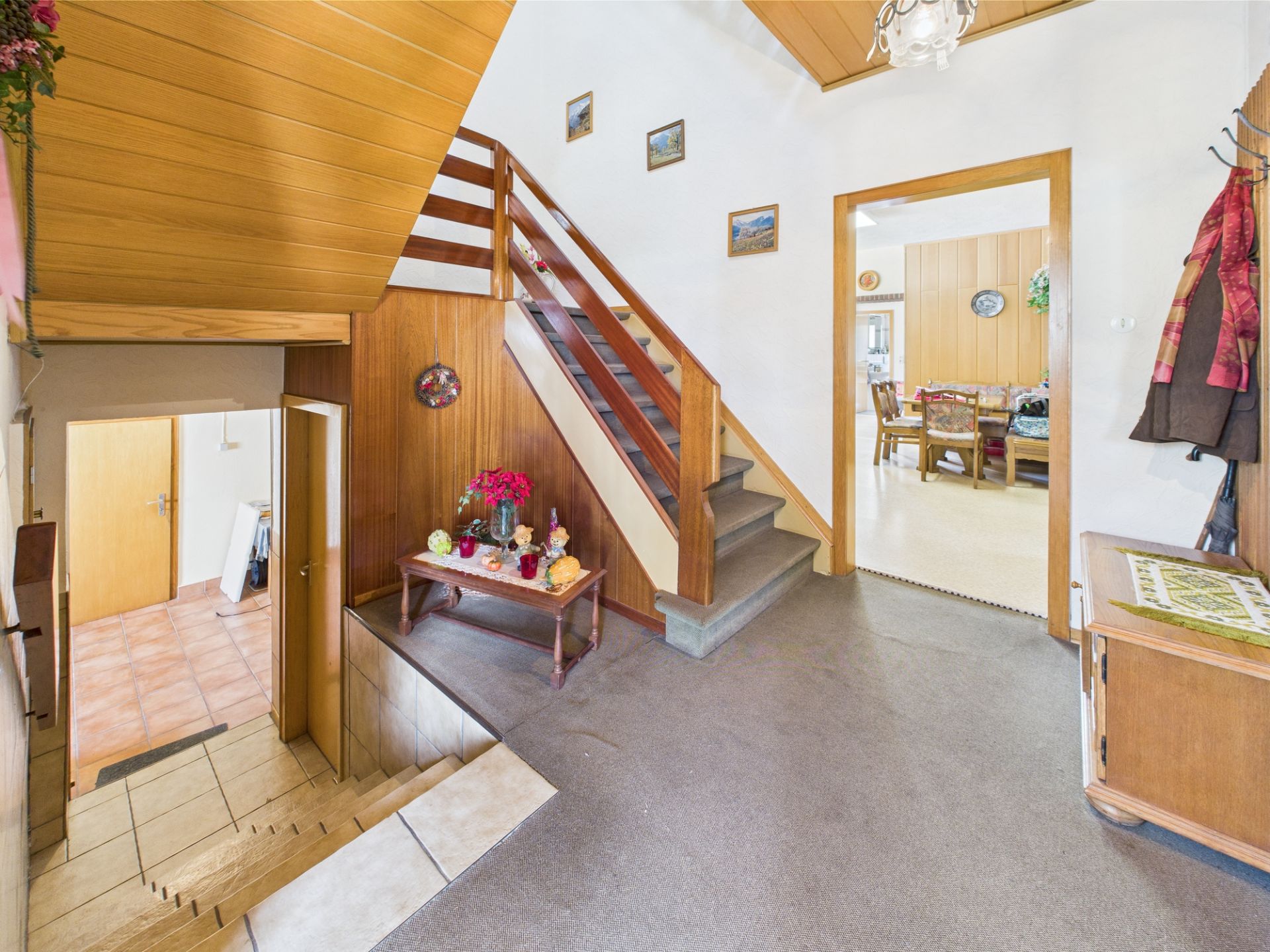 Flur mit Treppe, Dekotisch und Blick ins Esszimmer, Holzdecke und Wandvertäfelung.