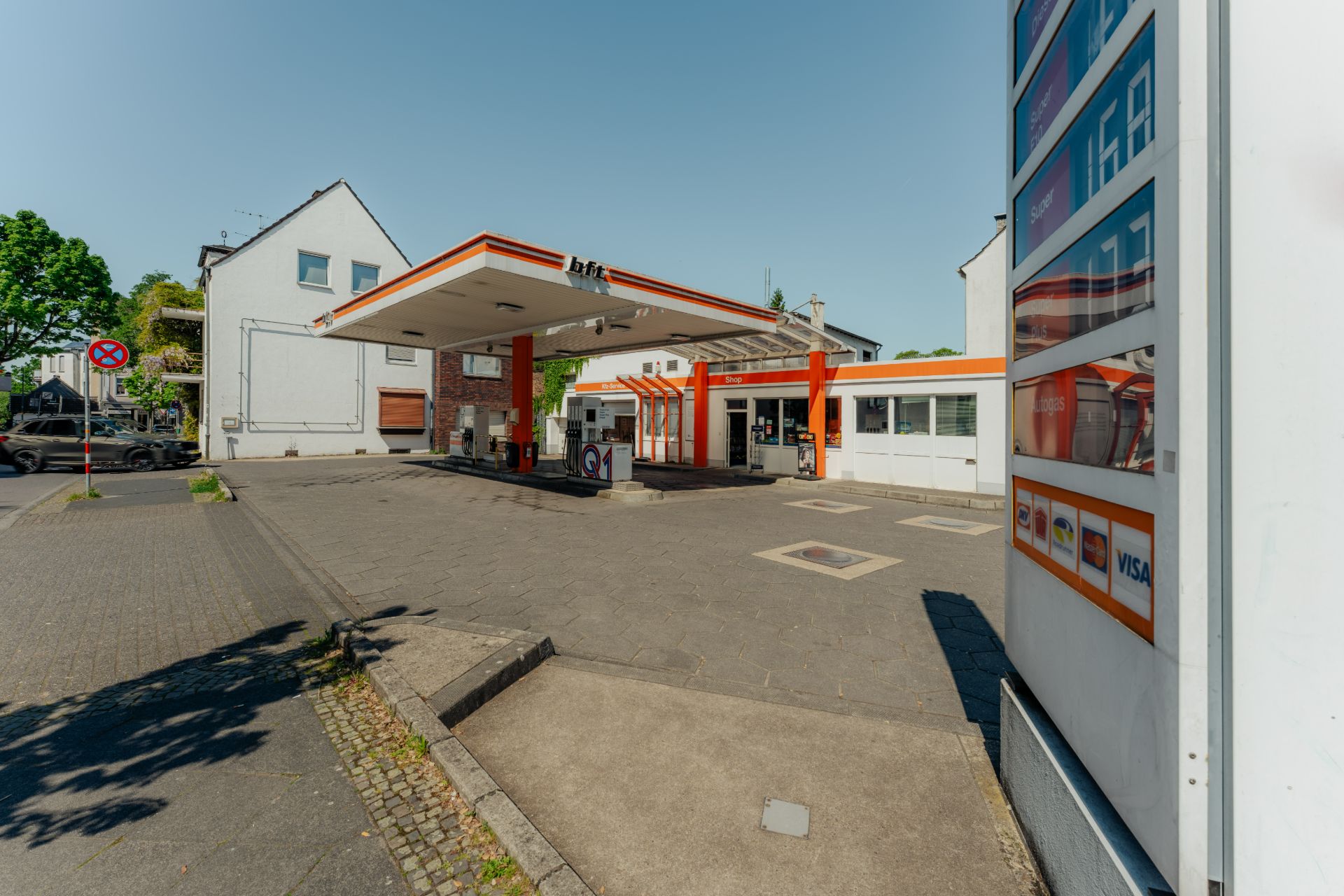 Außenansicht einer Tankstelle mit überdachter Zapfsäule und Preisen an einer Tafel.