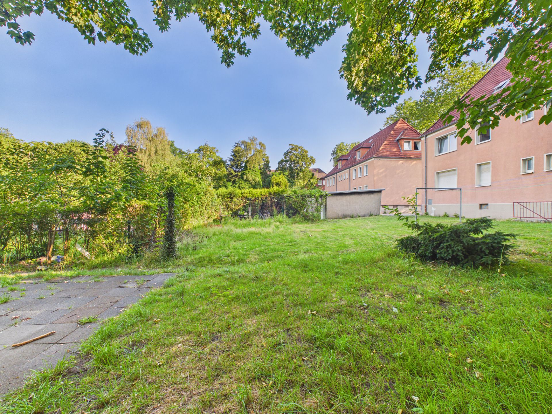 Grüner Garten mit Rasen und einigen Bäumen neben einem beigen Wohnhaus.