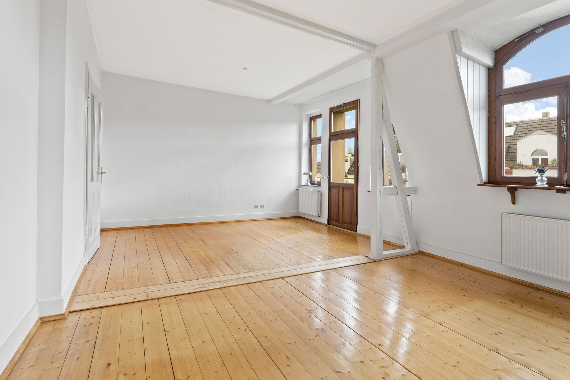Helles, leeres Zimmer mit Holzboden und großen Fenstern in einer Wohnung.
