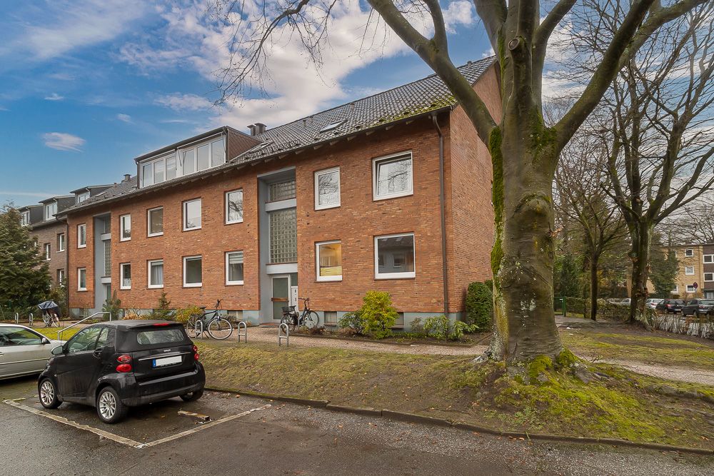 Mehrfamilienhaus mit Backsteinfassade, geparkten Autos und Fahrrädern vor dem Eingang.