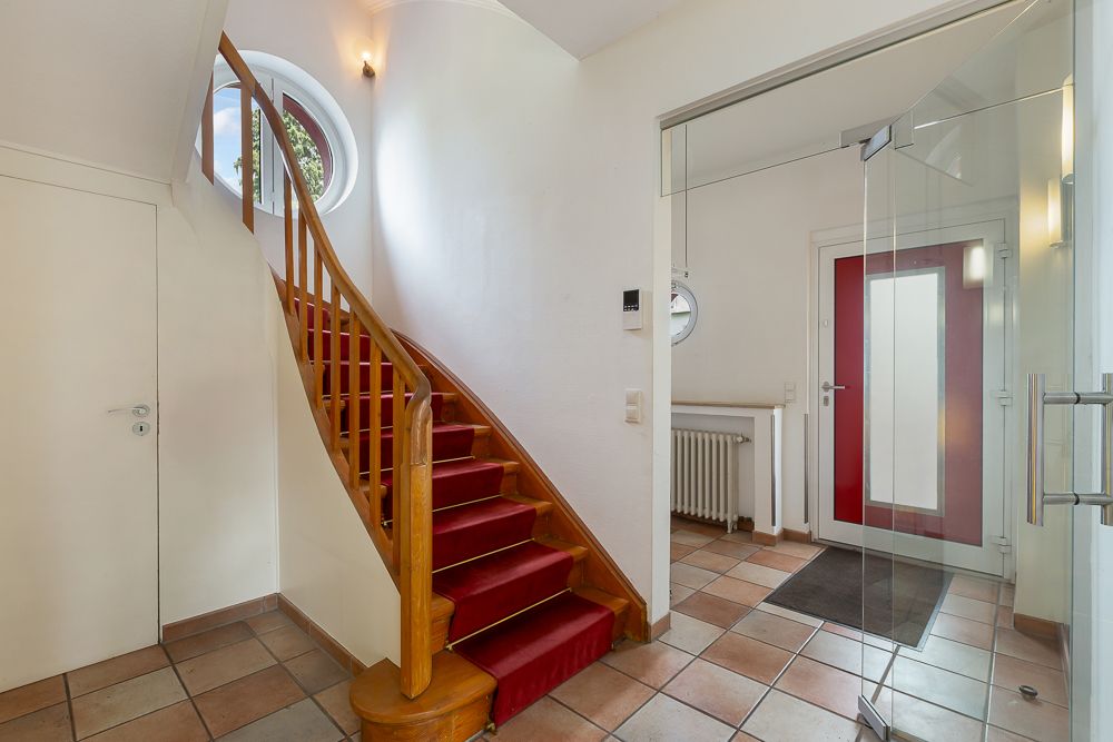 Eingangsbereich mit roter Treppe, Glastür und naturfarbenen Fliesenboden.