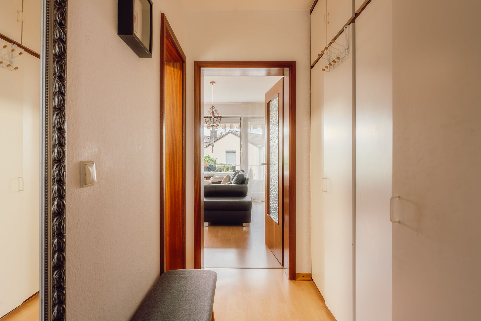 Heller Flur mit Spiegel, Garderobenschrank und Blick ins Wohnzimmer mit Sofa.