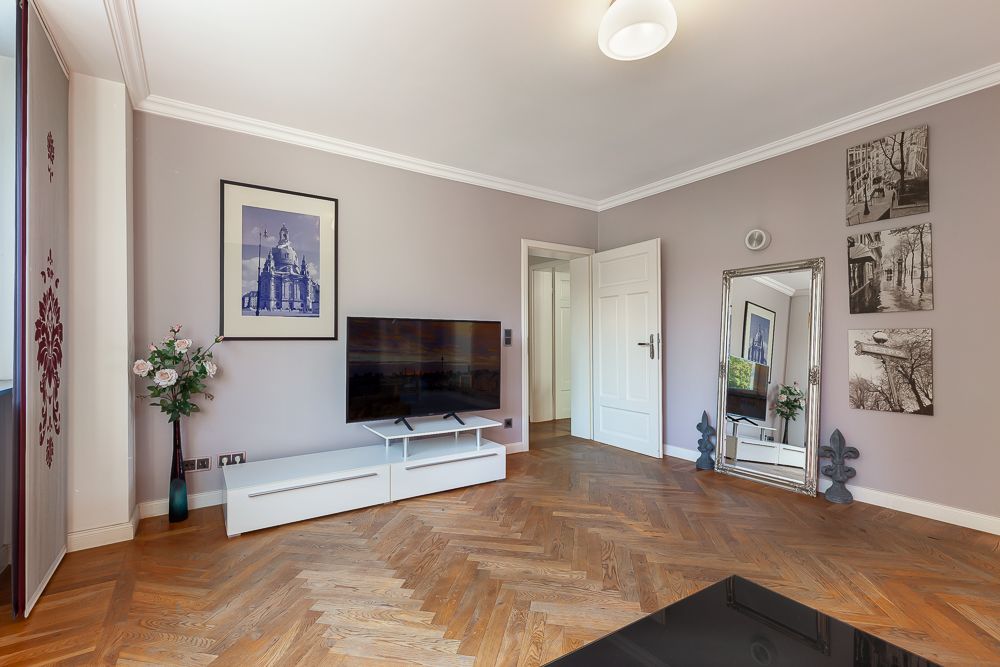 Modernes Wohnzimmer mit Holzfußboden, Fernseher, Spiegel und Wandbildern.
