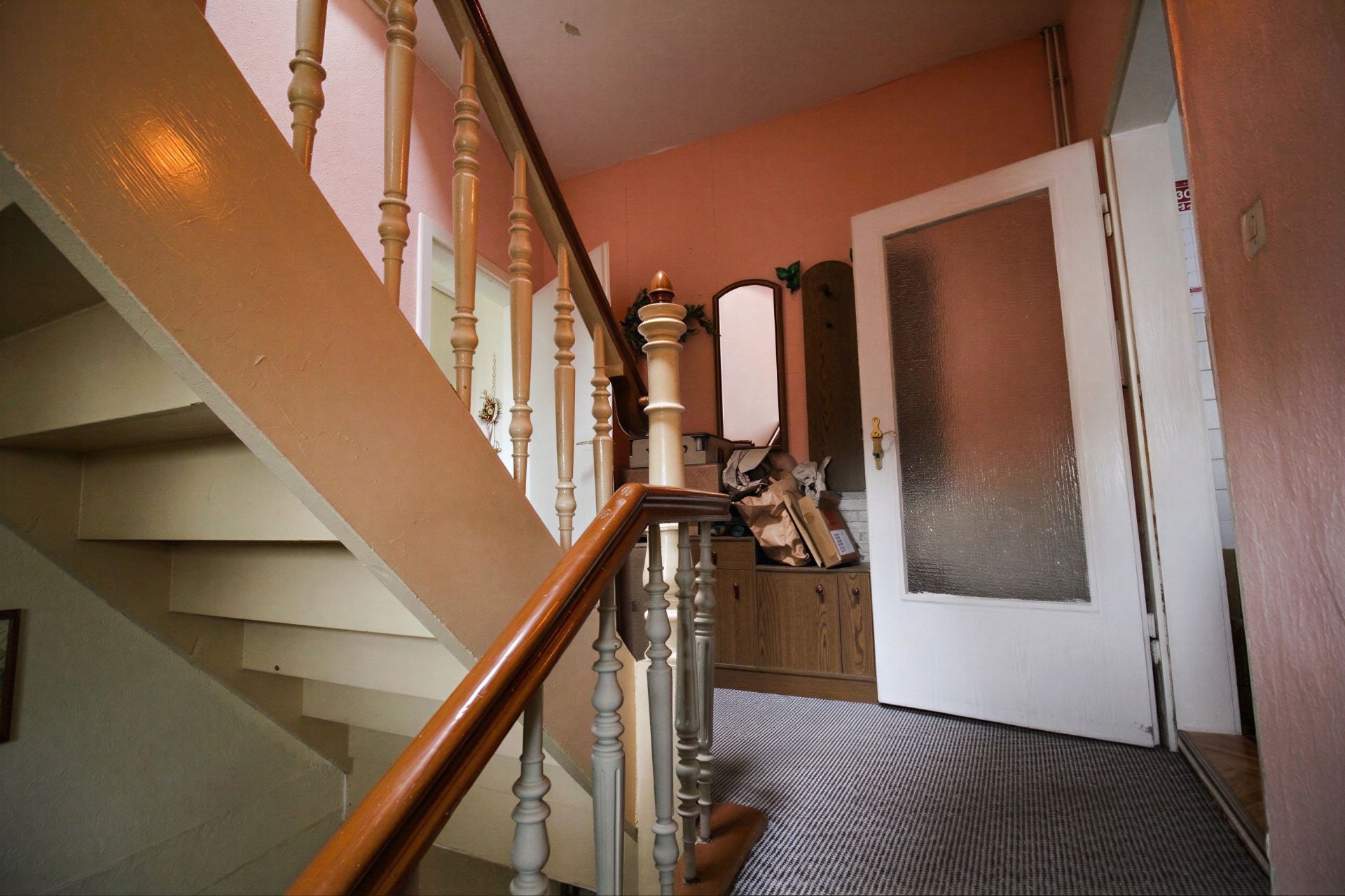 Flur mit Treppe, Teppichboden, offener Tür und Garderobe mit Spiegel.