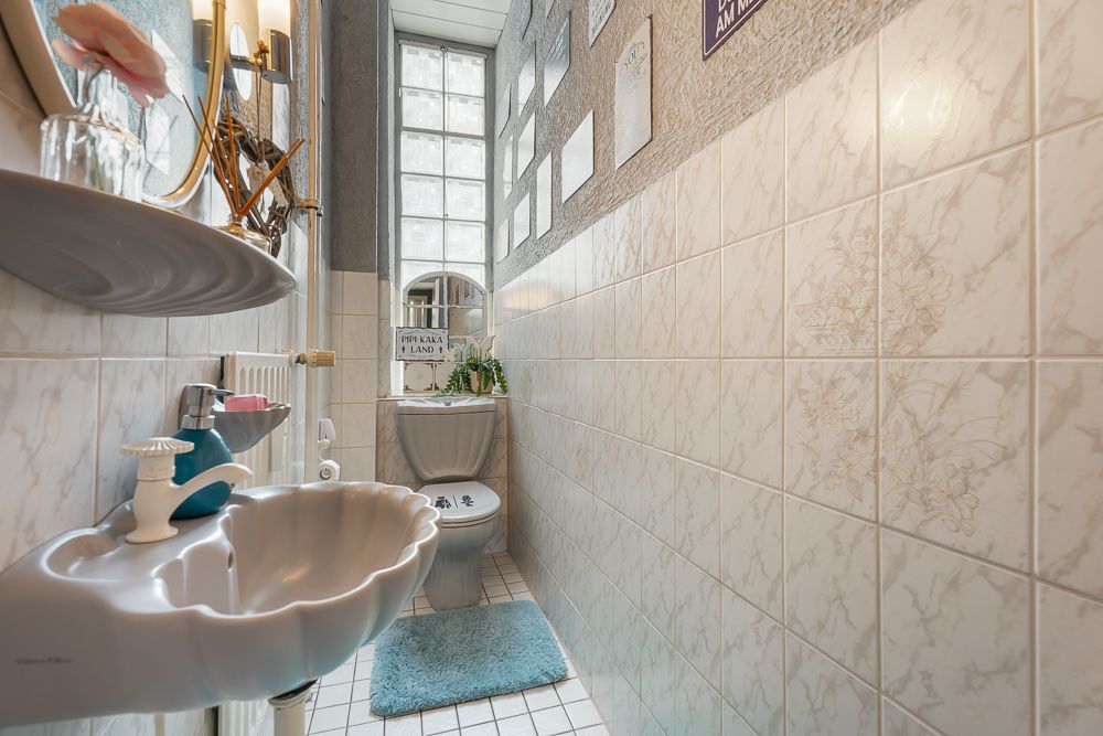 Schmales Badezimmer mit Waschbecken, Toilette und hellen Fliesen an den Wänden.