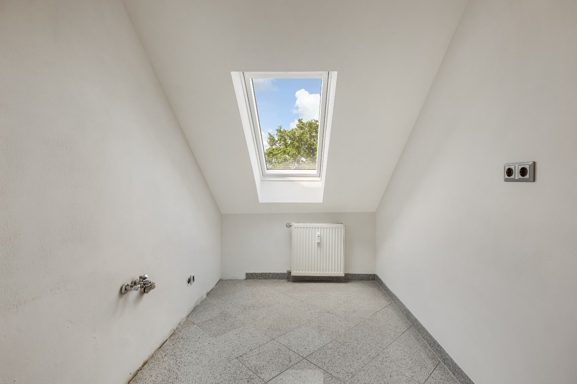Kleiner leerer Raum mit Dachfenster, Heizkörper und hellen Fliesen.