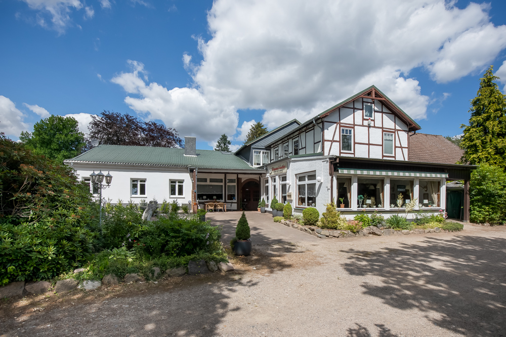 Großes weißes Wohnhaus mit Satteldach, Garten und Einfahrt bei sonnigem Wetter.