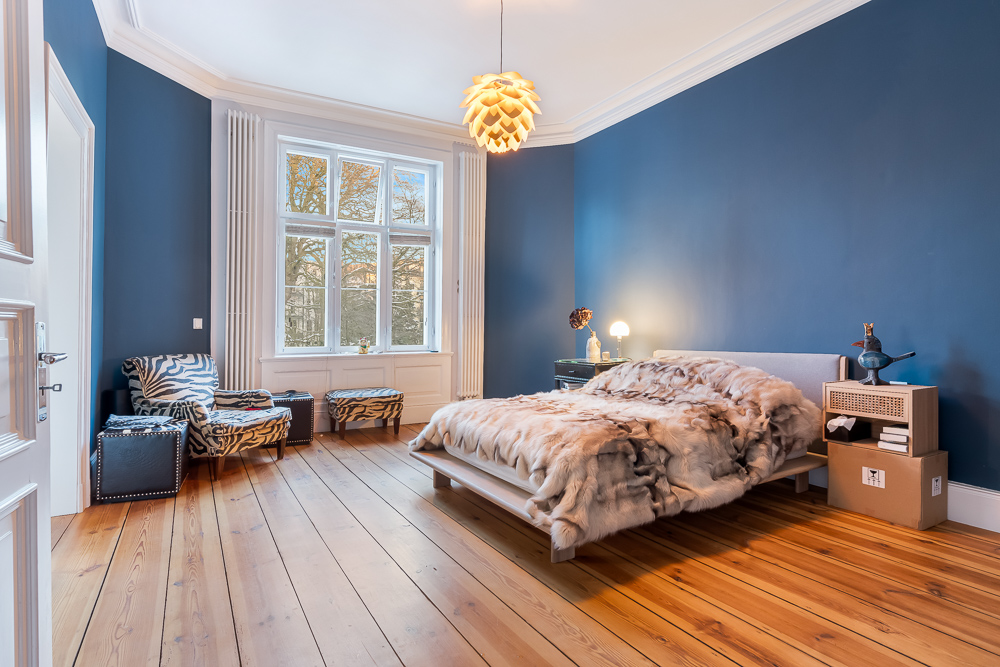 Modernes Schlafzimmer mit blau gestrichenen Wänden, großem Fenster und Holzboden.