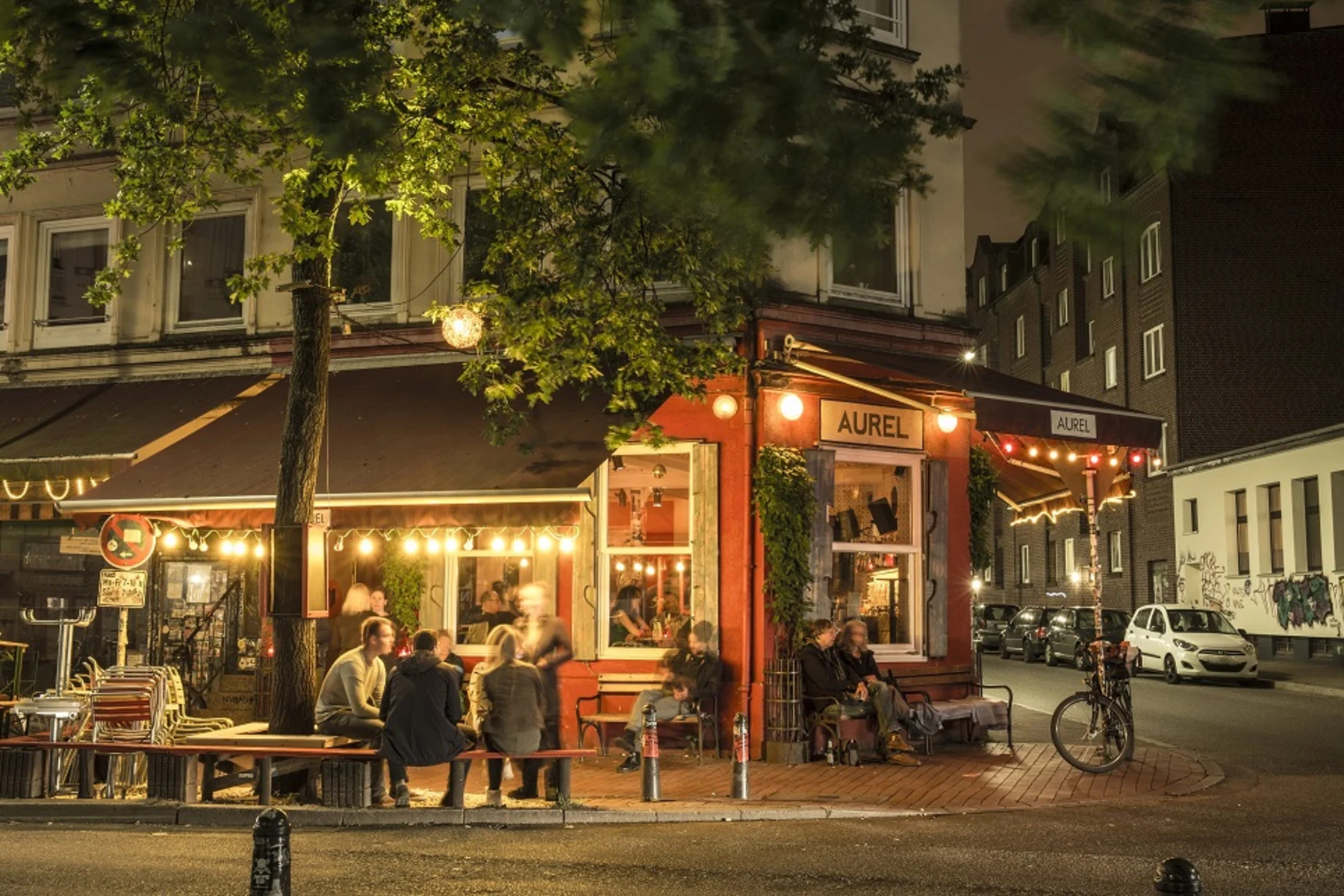 Gemütliches Straßencafé am Abend mit Menschen, die draußen unter Lichtern sitzen.