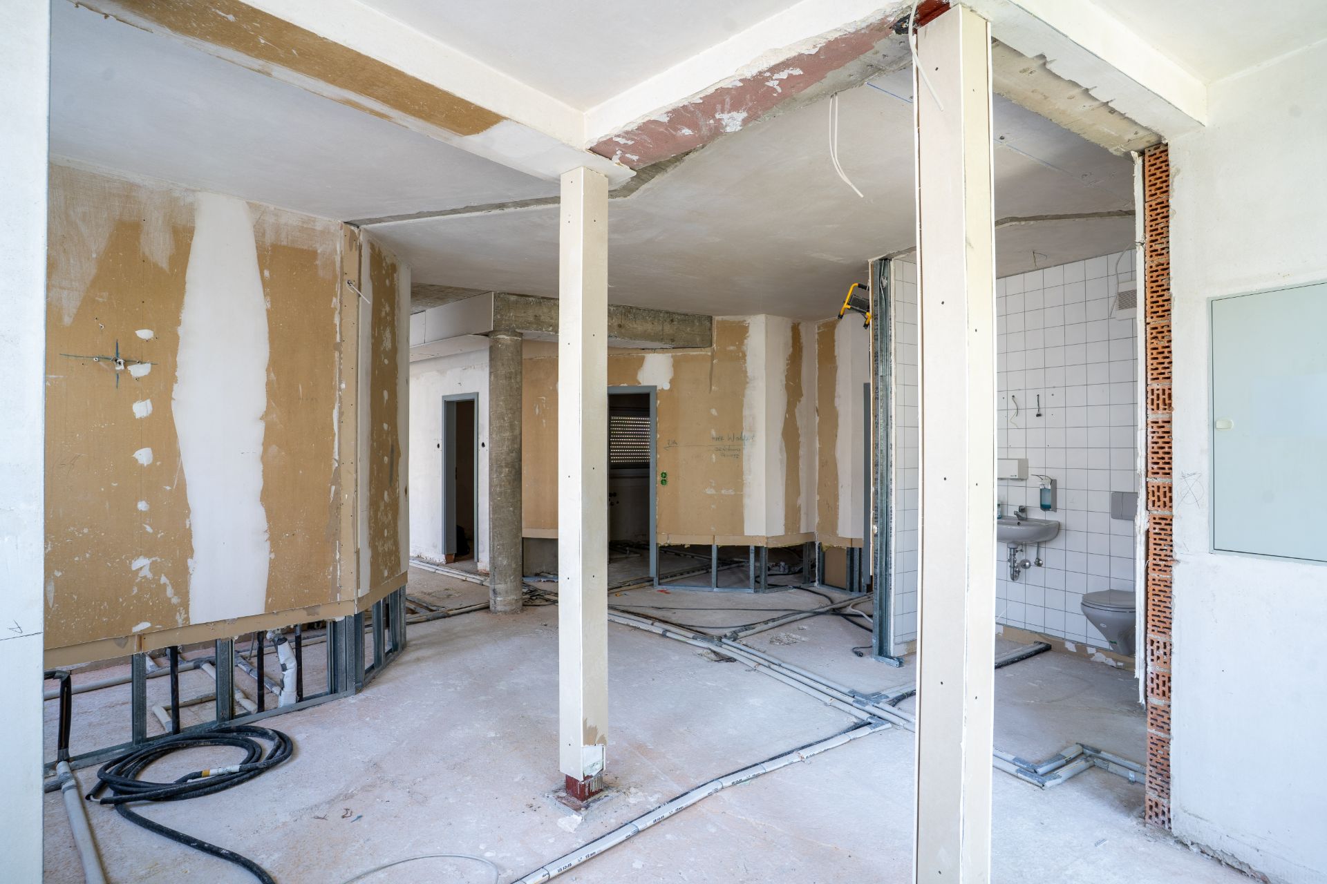 Raum im Rohbau mit freiliegenden Leitungen, offenen Wänden und einer kleinen Sanitäreinrichtung.