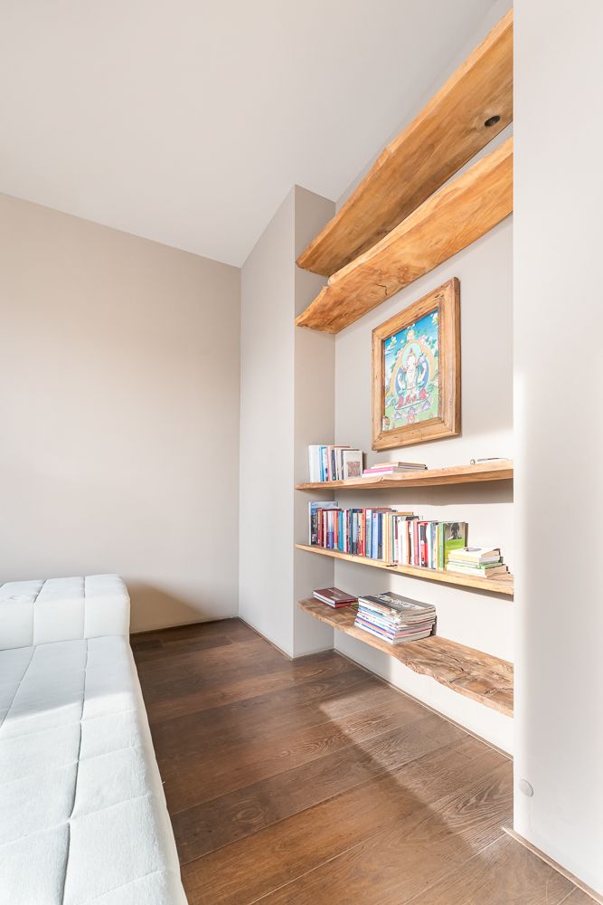 Helles Zimmer mit Holzregalen, Büchern, einem Bild an der Wand und einem weißen Sofa.