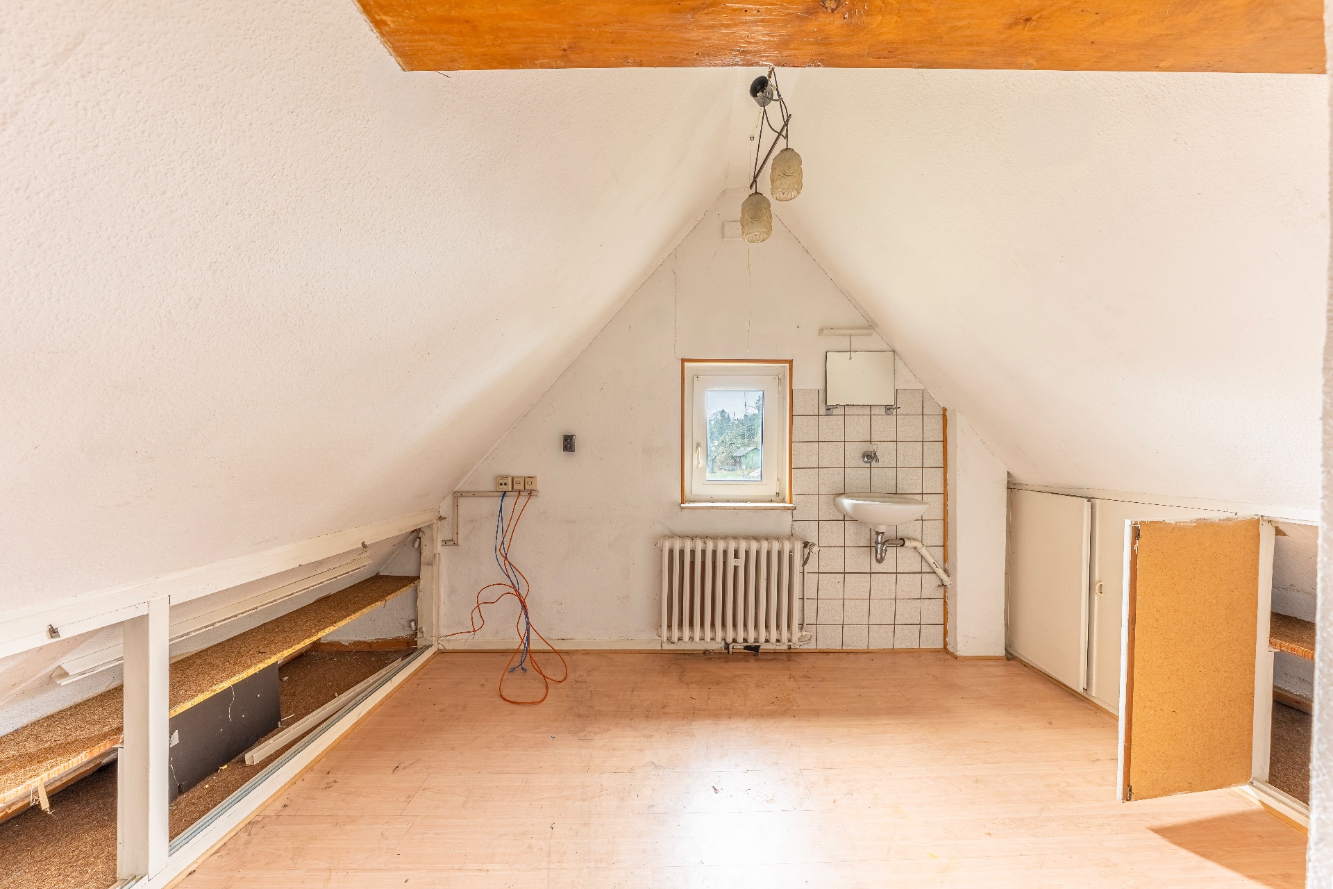 Dachzimmer mit schrägen Wänden, kleinem Fenster, Waschbecken und offenen Regalen.