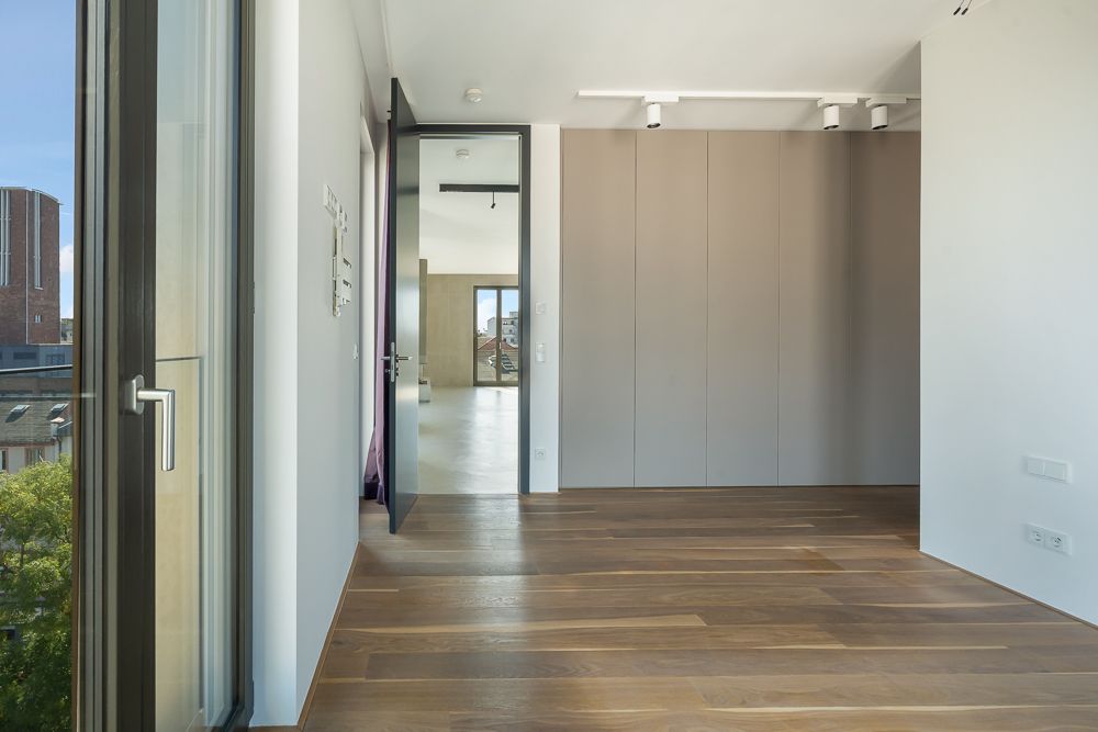 Helles Zimmer mit Holzboden, großen Fenstern und Einbauschrank, Blick in weiteren Raum.