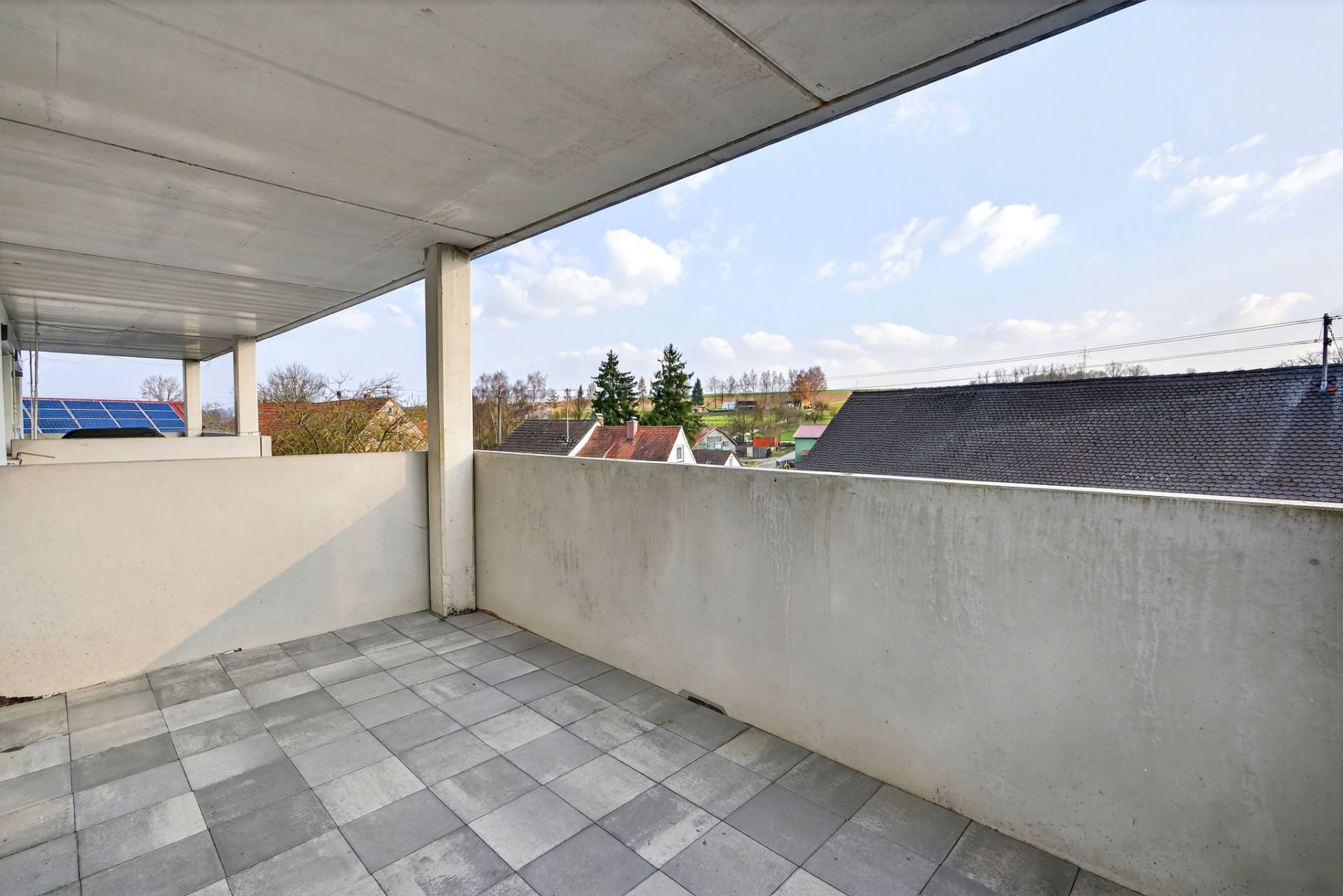 Überdachter Balkon mit Fliesenboden und Blick auf Dächer und Bäume.