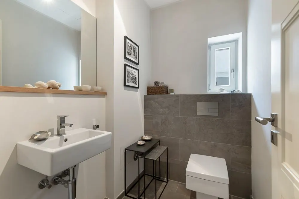 Modernes Badezimmer mit Wand-WC, kleinem Waschbecken, Spiegel und dekorierten Regalen.