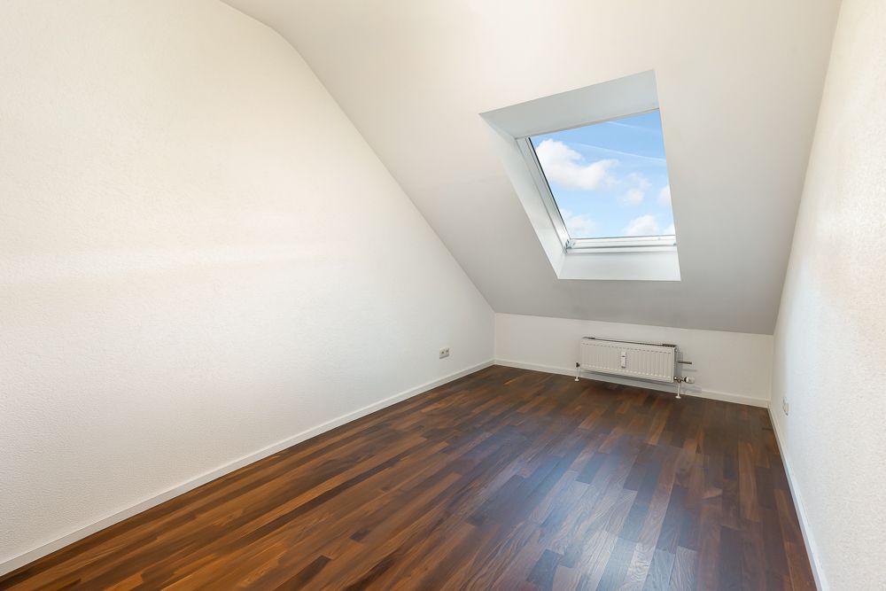 Leerer Raum mit Dachschräge, Holzfußboden und Fenster im Dach.