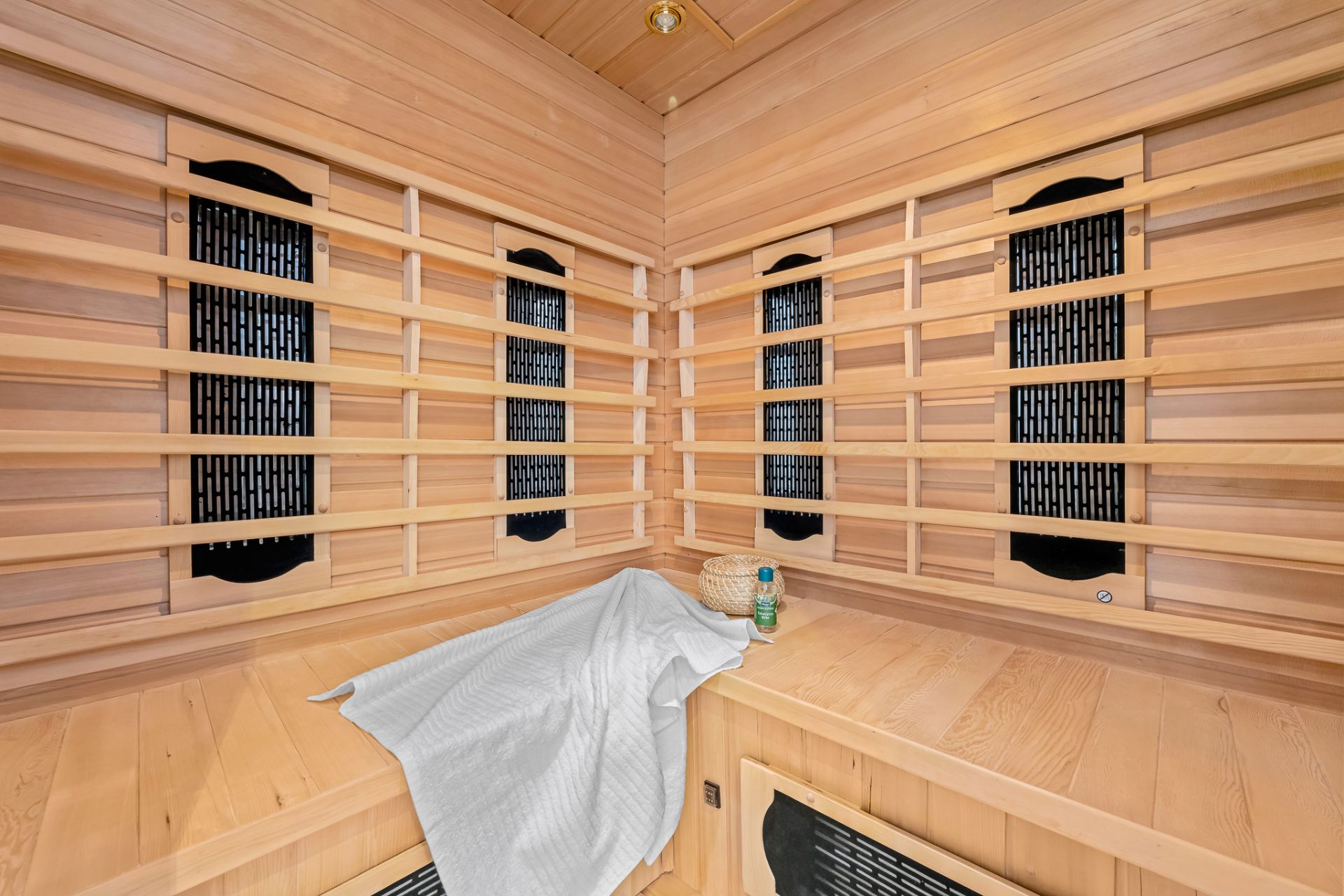 Innenraum einer modernen Sauna mit Holzverkleidung, Bank, Handtuch, Flasche und kleinem Korb.
