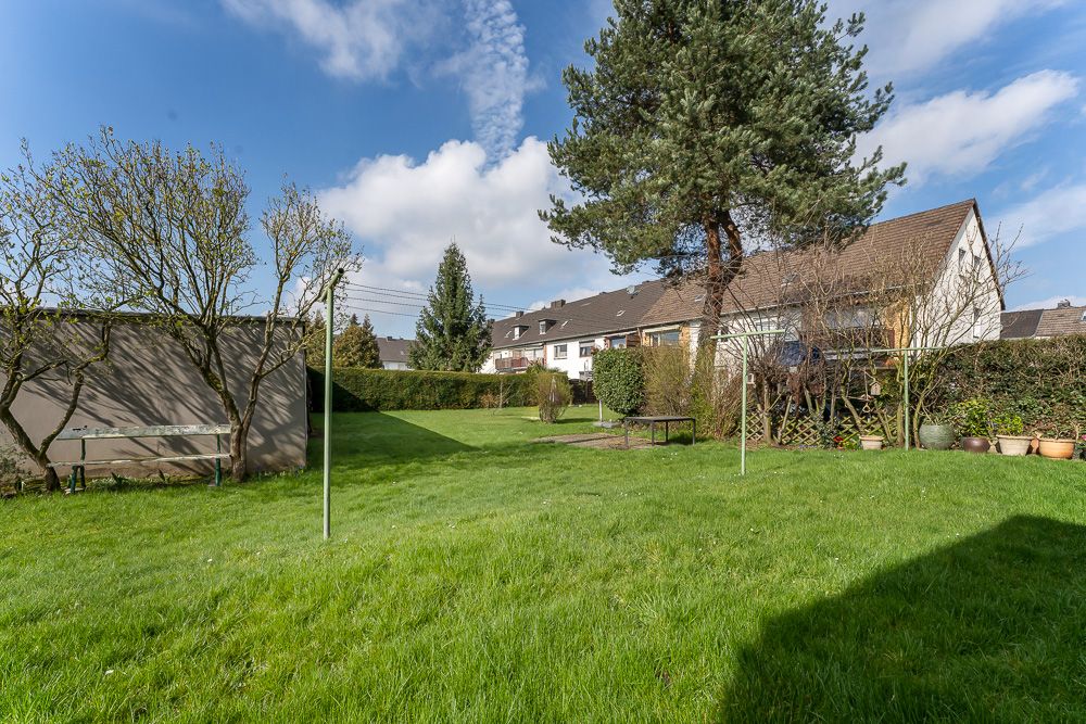 Großer grüner Garten mit Bäumen, einer Wäscheleine und Reihenhäusern im Hintergrund.