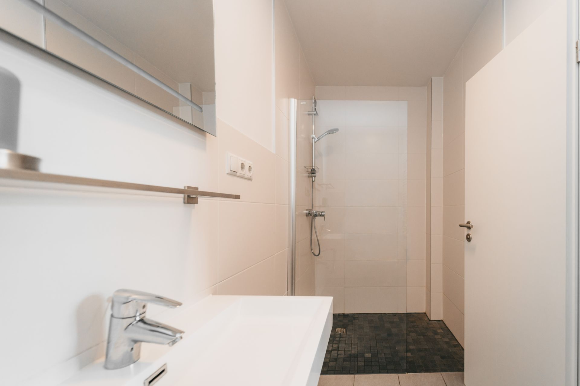 Modernes Badezimmer mit Waschbecken, Spiegel und ebenerdiger Dusche.