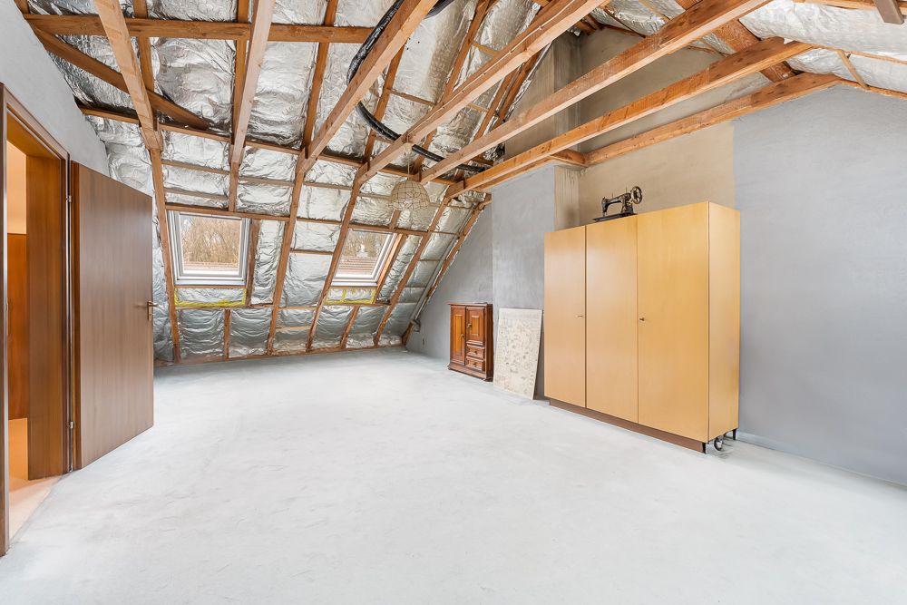 Heller Dachbodenraum mit sichtbaren Balken, zwei Dachfenstern, Schrank und Kommode.