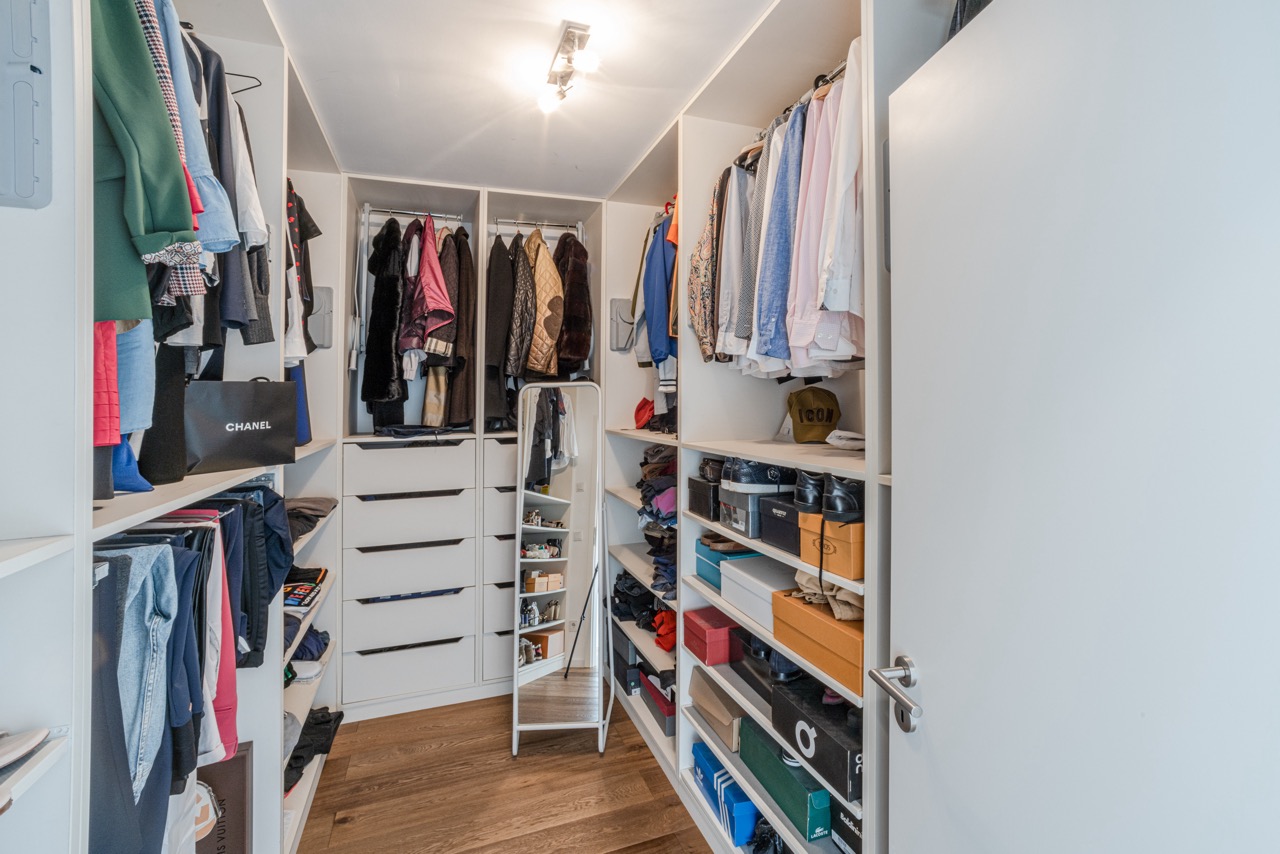 Begehbarer Kleiderschrank mit Regalen, Hängestangen, Kleidung und einem Spiegel.