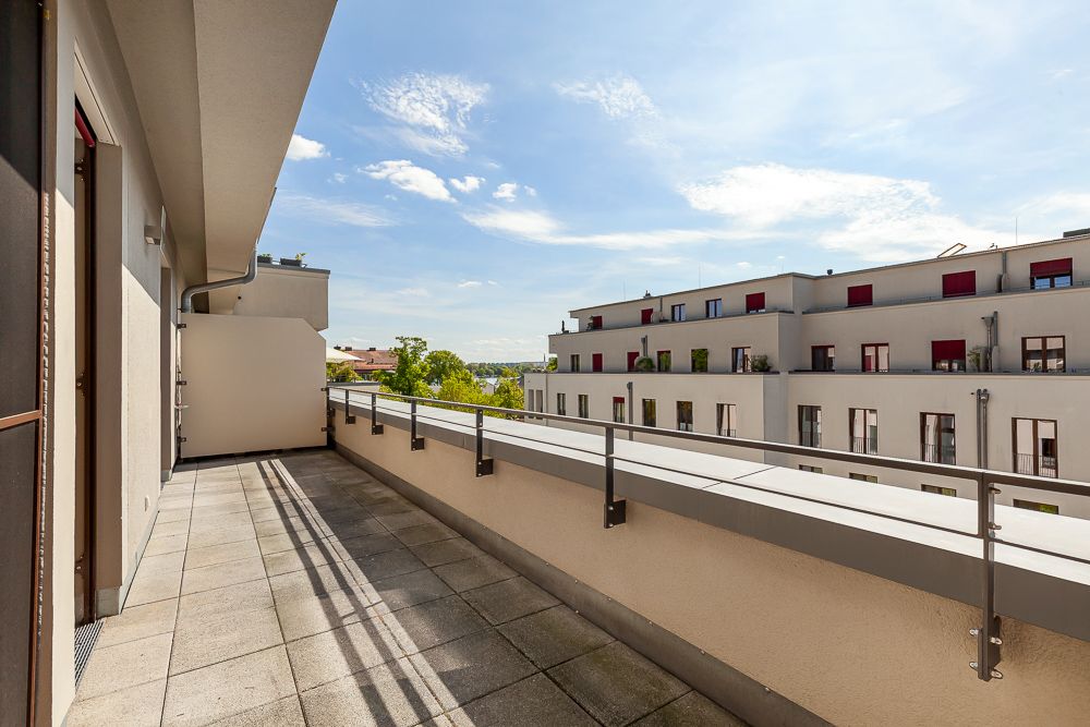 Großer Balkon mit Fliesenboden und Blick auf modernes Wohngebäude bei sonnigem Wetter.