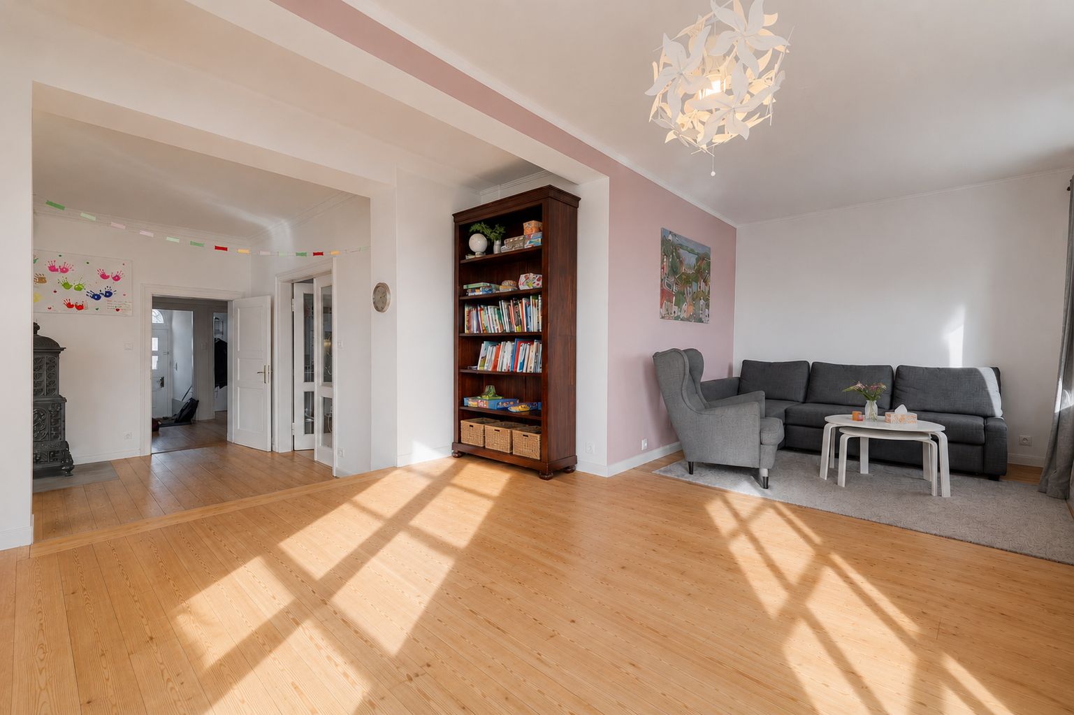 Helles Wohnzimmer mit Holzfußboden, Bücherregal und Sitzecke mit Sofa und Sessel.