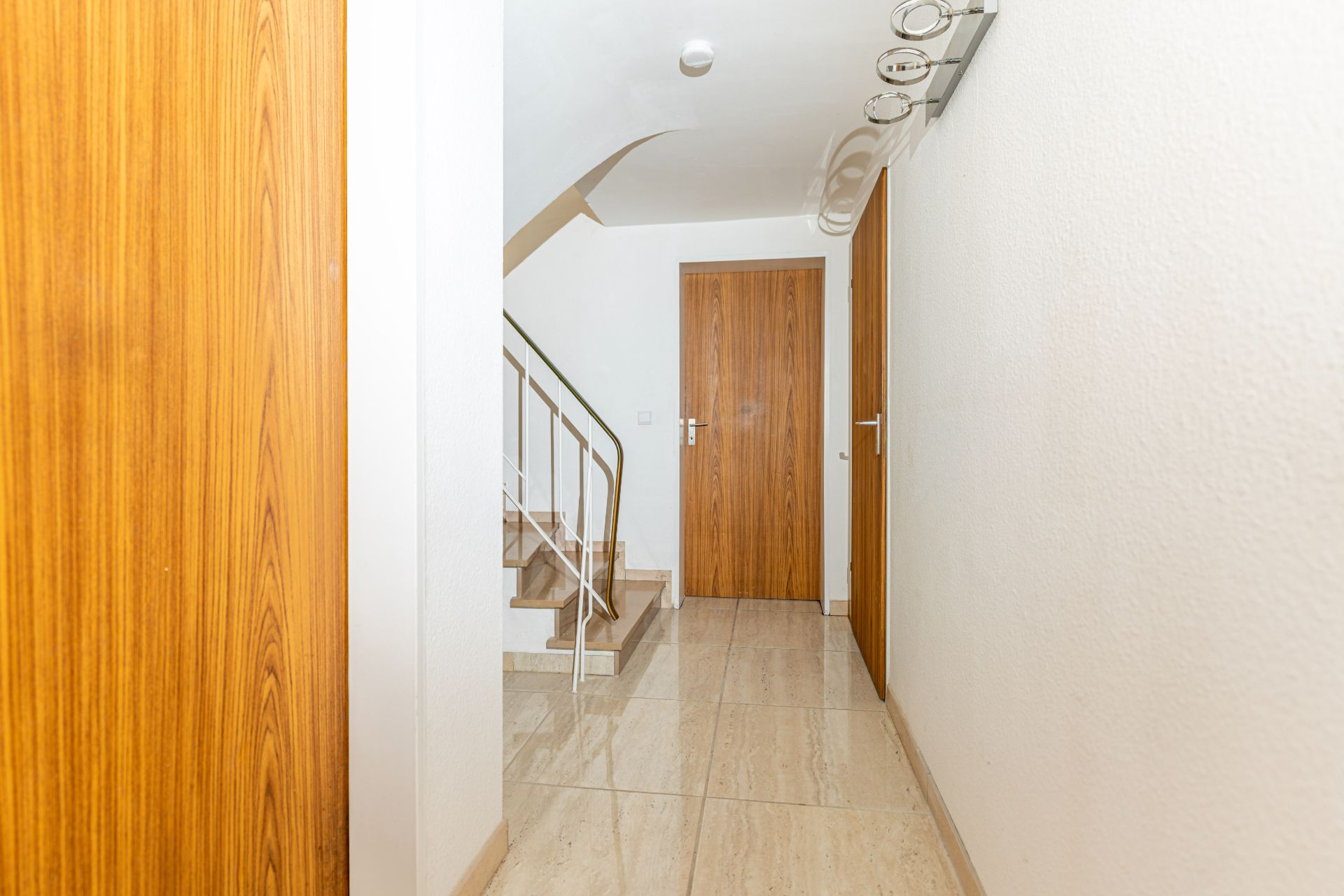 Heller Flur mit Fliesenboden, Holztüren und Treppe mit Metallgeländer.