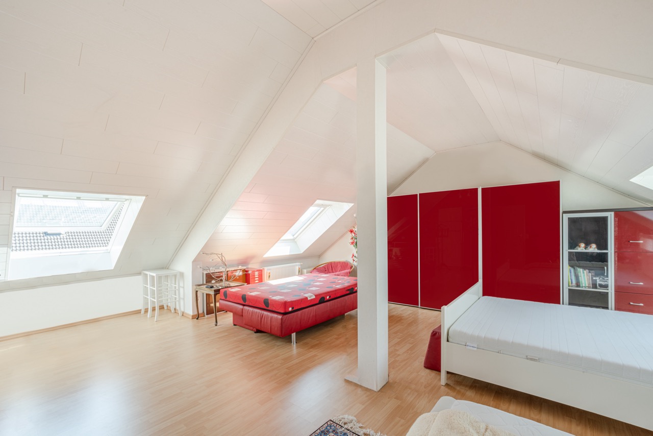 Helles Zimmer im Dachgeschoss mit zwei Betten, roten Schränken und schrägen Dachfenstern.