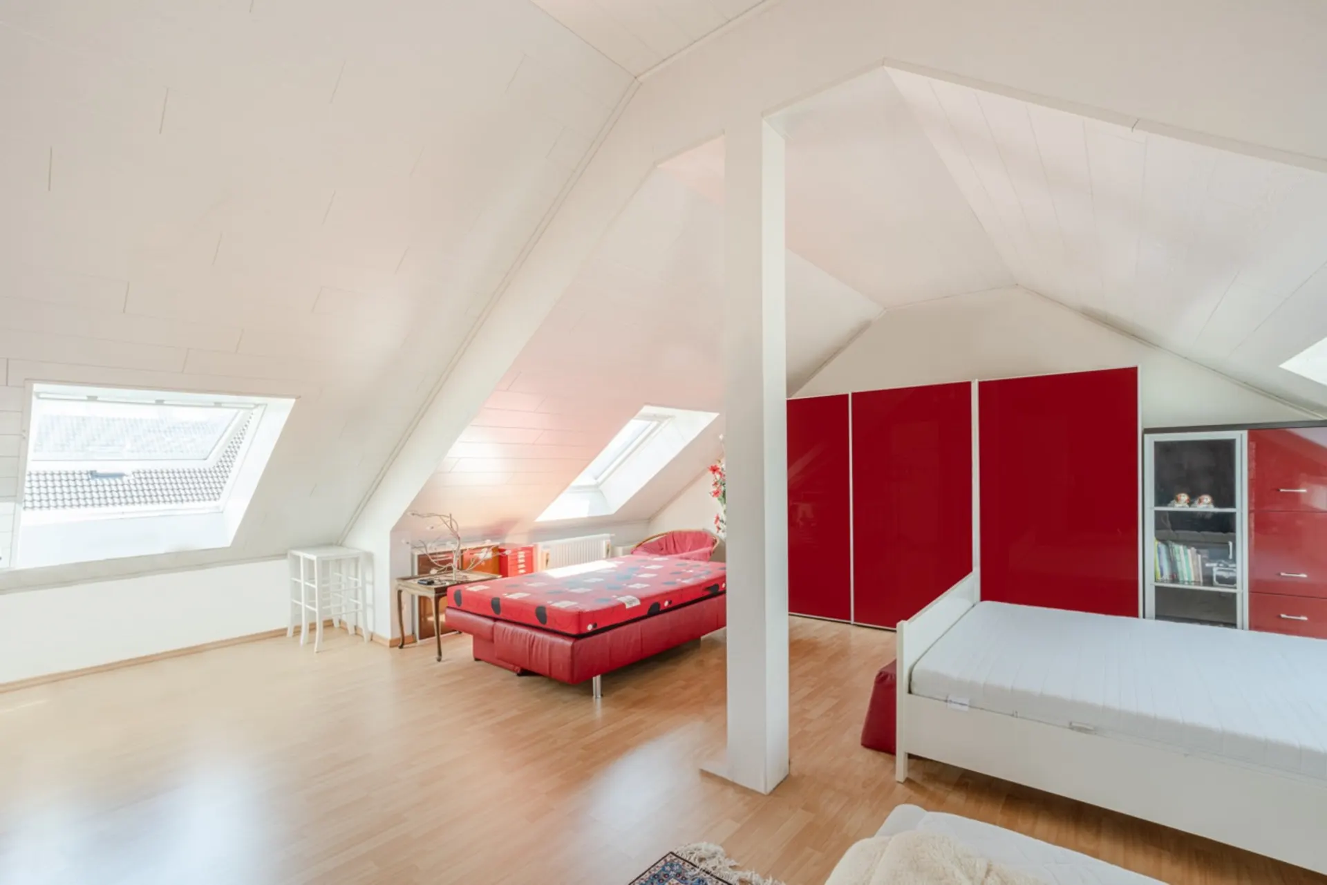 Helles Zimmer im Dachgeschoss mit zwei Betten, roten Schränken und schrägen Dachfenstern.