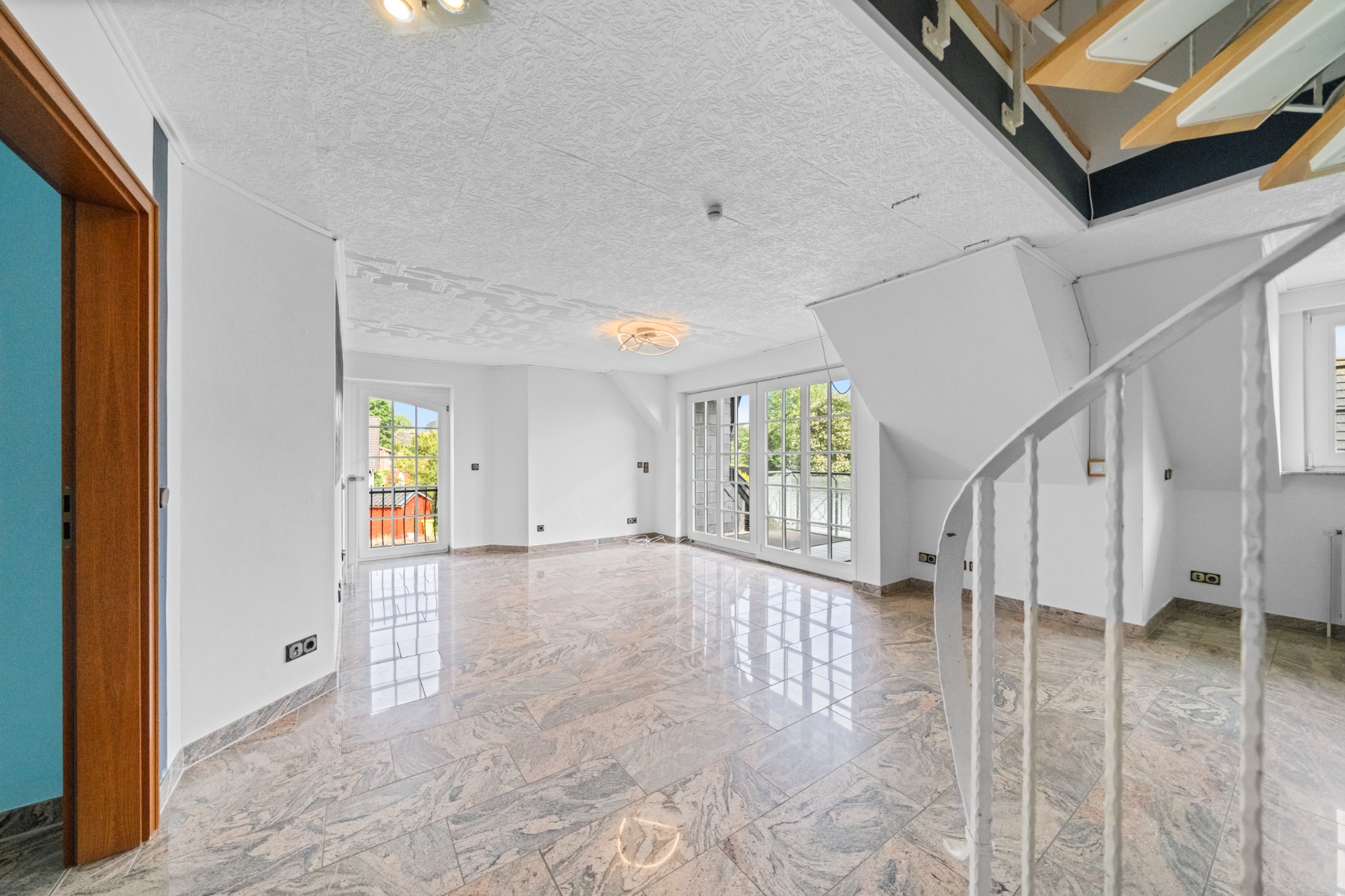 Heller Wohnraum mit Marmorboden, großen Fenstern und offener Treppe, Blick auf Terrasse.