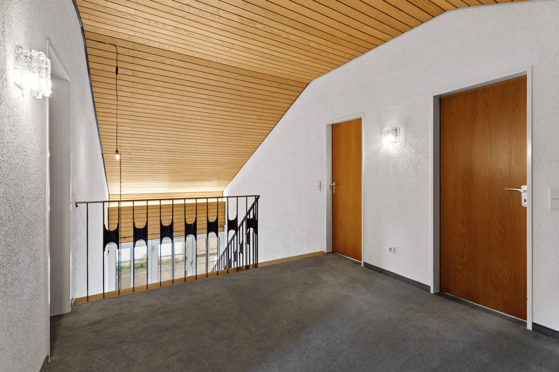 Flur mit Teppichboden, Holzdecke, zwei Holztüren und Treppengeländer.