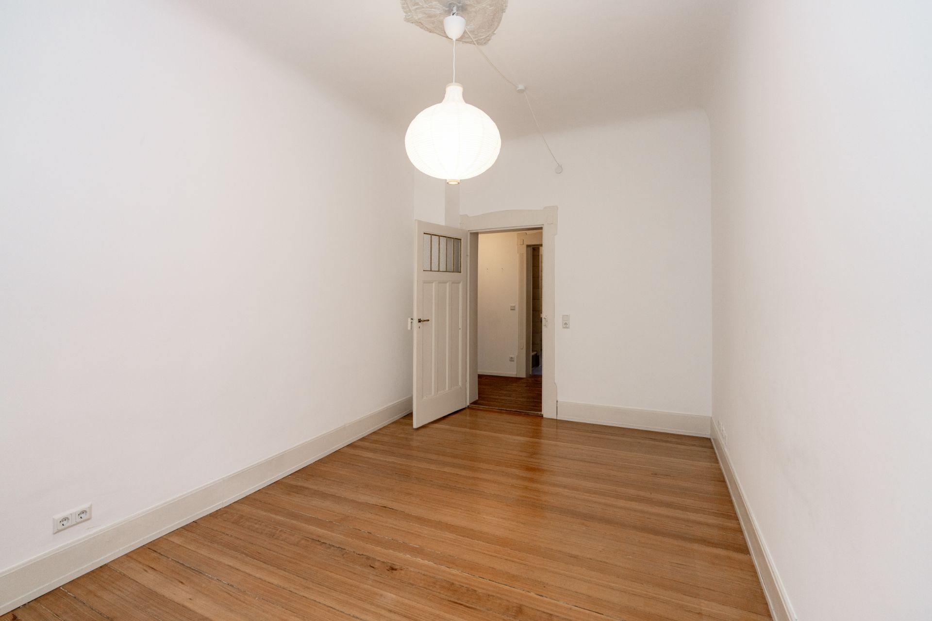 Leerer Raum mit Holzboden, weiß gestrichenen Wänden und geöffneter Tür.