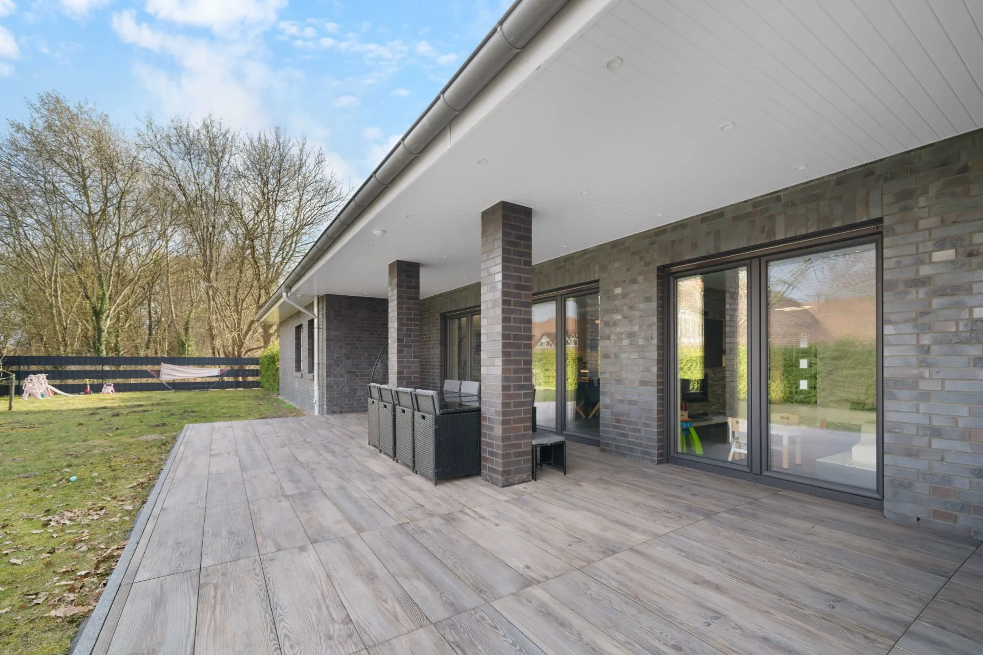 Moderne Terrasse mit überdachtem Bereich und Blick auf einen großen Garten mit Bäumen.