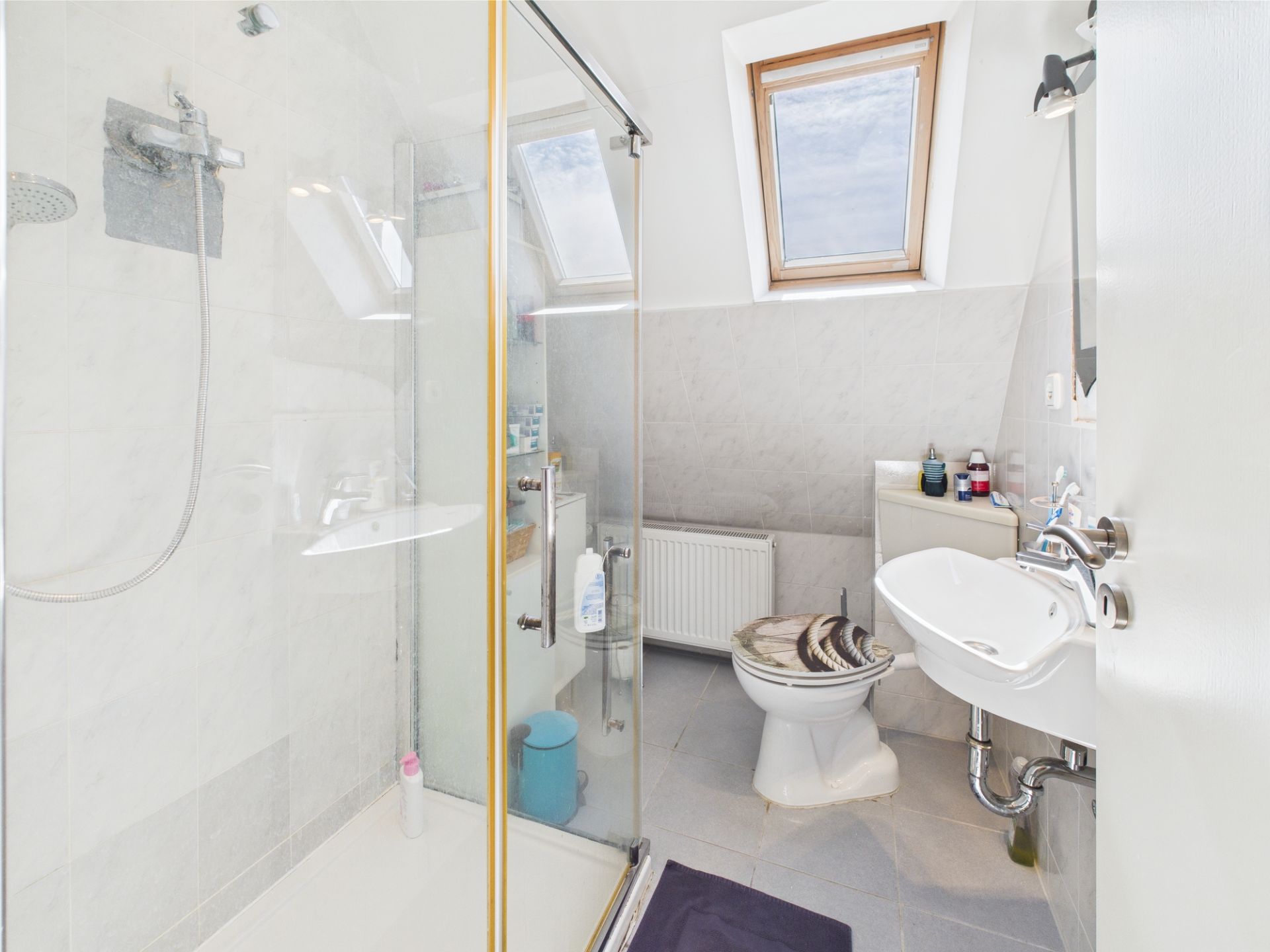 Helles Badezimmer mit Dusche, Toilette, Waschbecken und zwei Dachfenstern.