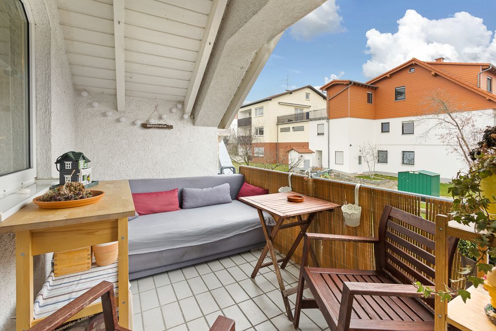 Gemütlicher Balkon mit Sofa, Holztisch, zwei Stühlen und Blick auf Nachbarhäuser.