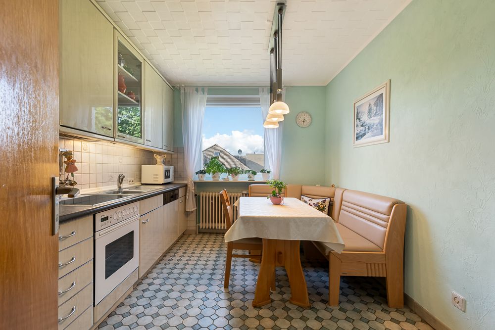 Helle Küche mit Einbauküche, Eckbank, Esstisch und großem Fenster mit Blick nach draußen.