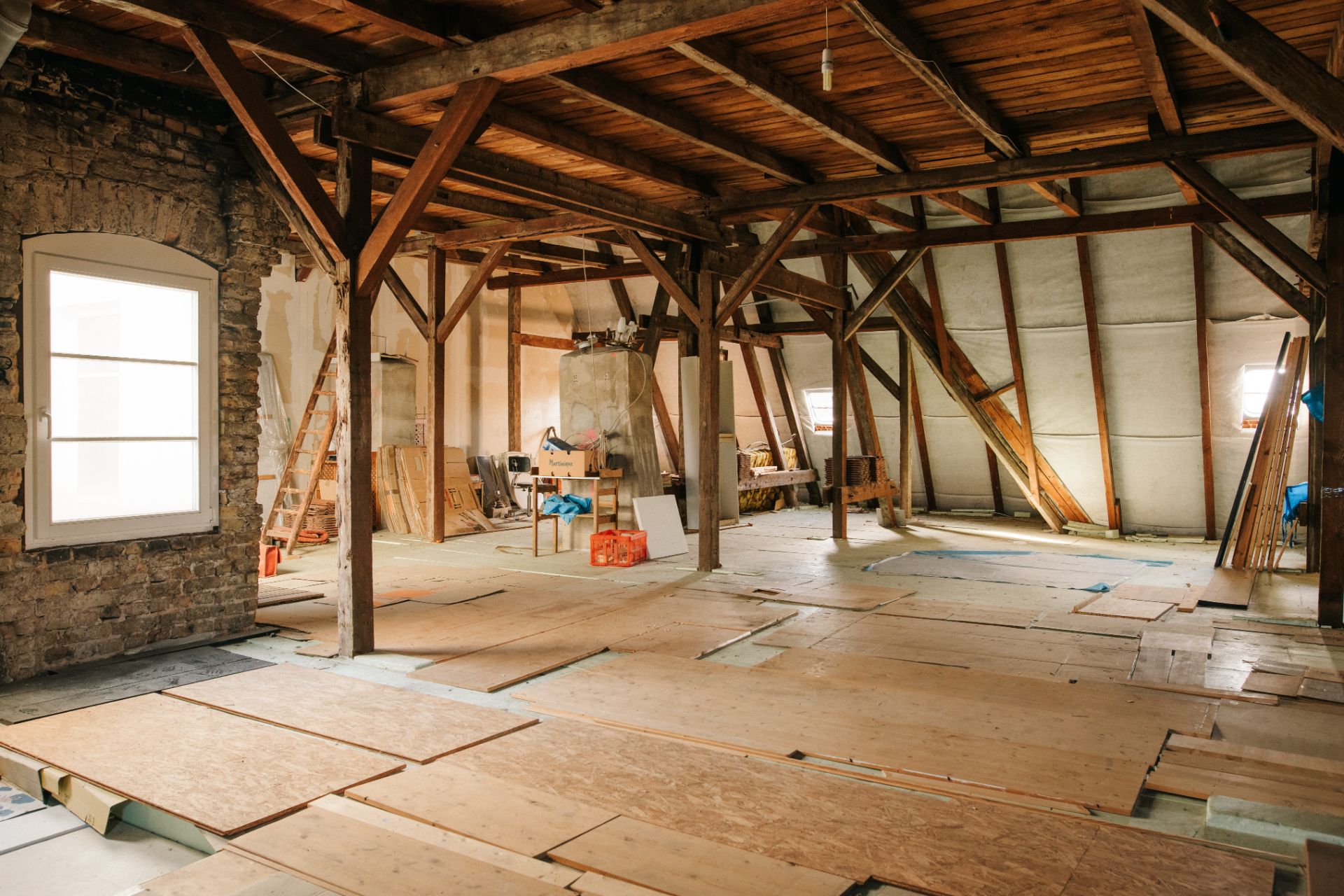 Dachboden mit Holzbalken und Brettern, teilweise renoviert, Baumaterialien sichtbar.