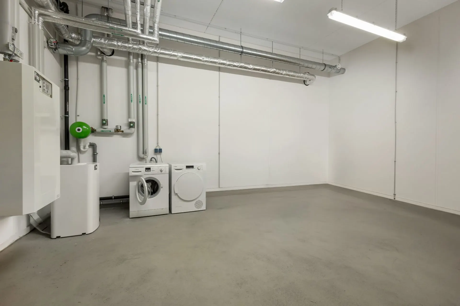 Hauswirtschaftsraum mit Waschmaschine, Trockner und sichtbaren Rohrleitungen an der Wand.