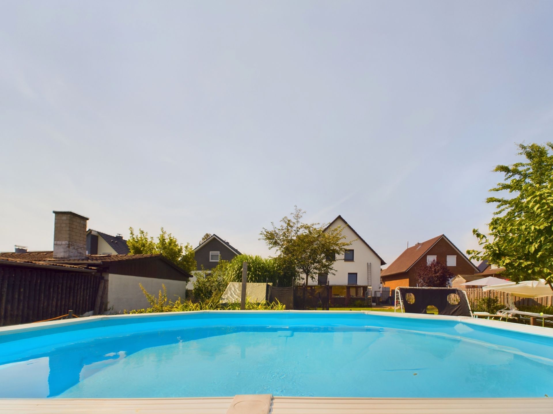 Ein runder Pool im Garten mit Blick auf mehrere Wohnhäuser im Hintergrund.