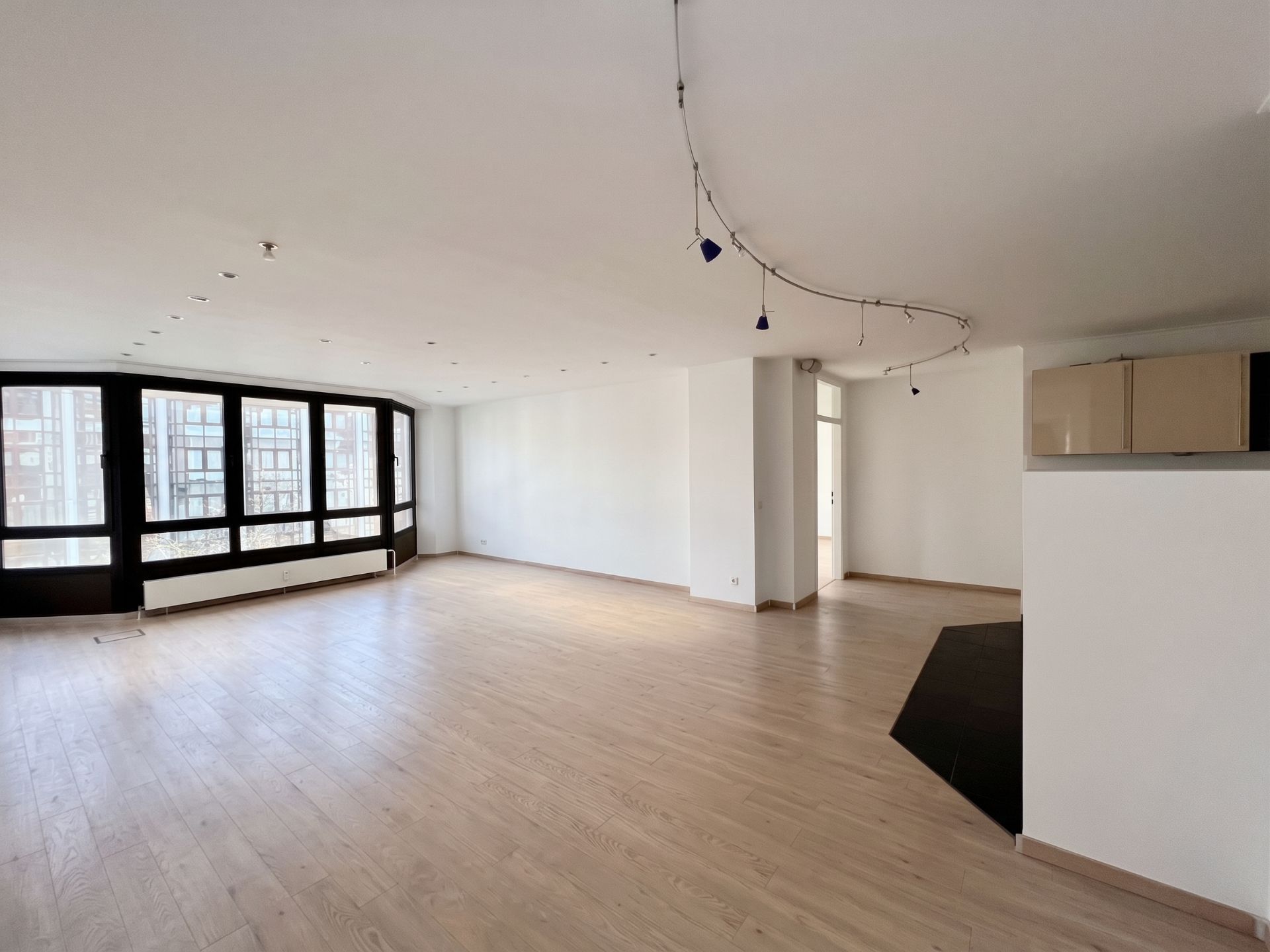Helles, leeres Wohnzimmer mit großen Fenstern und Holzfußboden.