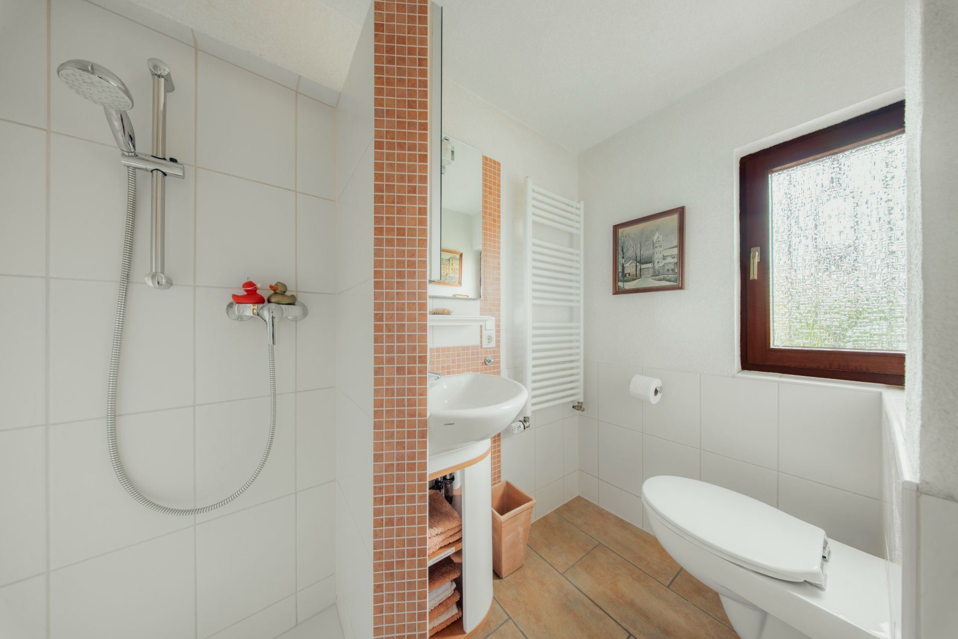 Helles Badezimmer mit Dusche, Waschbecken, WC, Fenster und Wandheizkörper.
