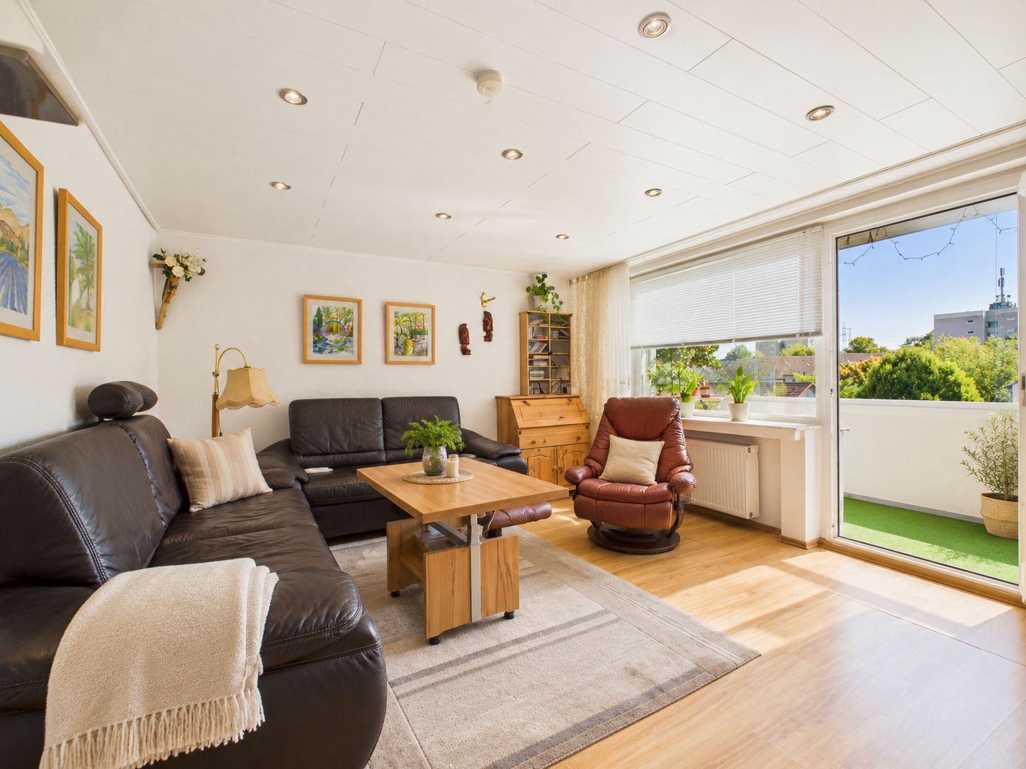Helles Wohnzimmer mit Ledersofas, Couchtisch, Sessel und Zugang zum Balkon.